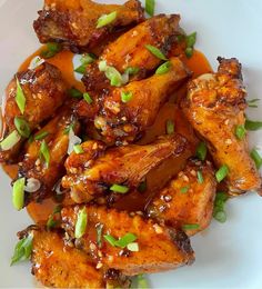 a white plate topped with chicken wings covered in sauce and garnished with green onions