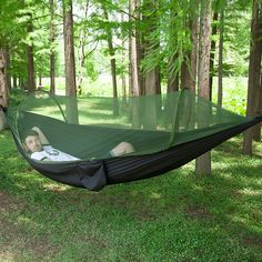 a man laying in a green hammock with trees behind him and grass on the ground