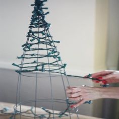 two hands are decorating a wire christmas tree