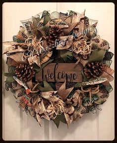 a welcome wreath with pine cones and ribbons hanging on the front door for someone to welcome