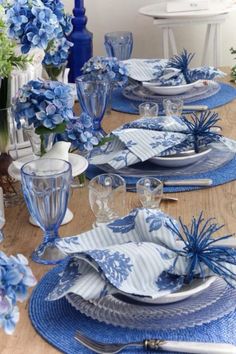 a blue and white table setting with flowers in vases on the side, plates and silverware