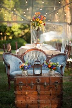 an old trunk is sitting in the grass near a table with flowers and candles on it