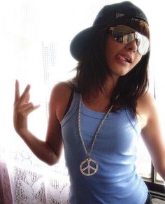 a woman wearing sunglasses and a hat with peace sign on it's chest standing in front of a window