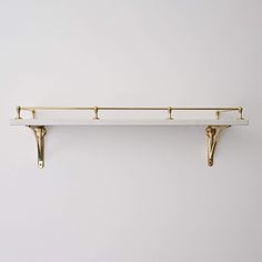 a white shelf with two gold hooks on it