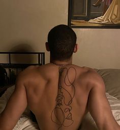 a man with a tattoo on his back sitting in bed