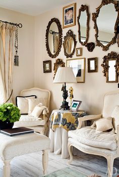 a living room filled with white furniture and lots of mirrors on the wall above it