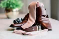 a pair of brown shoes with a pink tie and eyeglasses sitting on a table