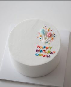 a white birthday cake with colorful sprinkles and balloons