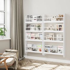 a white book shelf sitting next to a window in a living room with a chair