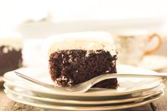 a piece of chocolate cake on a plate with a fork and cup in the background