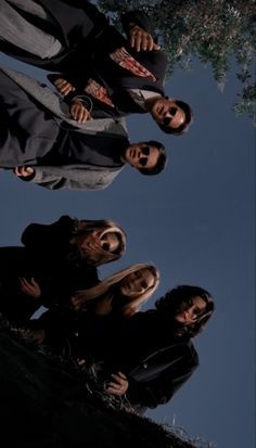 three people standing in front of a tree looking up at the sky with their hands on their hipss