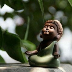 a small buddha statue sitting on top of a stone wall next to green plants and leaves