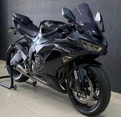 a black motorcycle is parked in front of a gray wall and some tile flooring