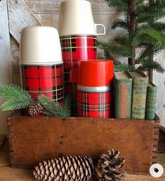 some pine cones are sitting in a wooden box with red and white plaid coffee mugs