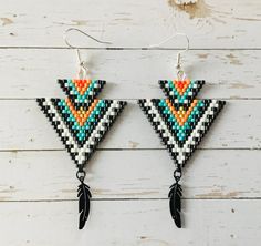 two pairs of beaded earrings with feathers hanging from them on a white wooden surface