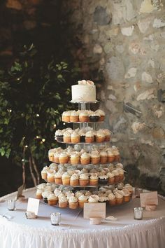 a wedding cake and cupcakes on a table in front of a stone wall