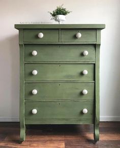 a green dresser with white knobs on it's top and bottom drawers, in front of a wall