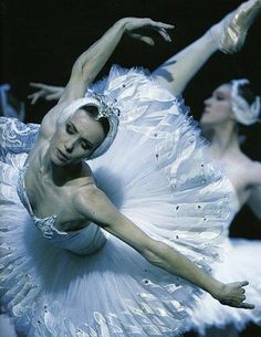 two ballerinas in white tutus and tiaras, one holding her leg up