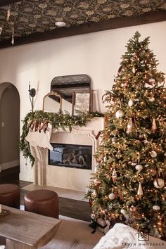 a living room decorated for christmas with a tree in the corner and stockings on the fireplace