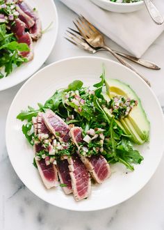 two white plates filled with food on top of a marble countertop next to a bowl of salad