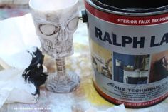 a can of paint next to a cup with a skull head on it and some tissue paper