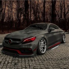 a car parked in front of some trees on a cobblestone road with black rims