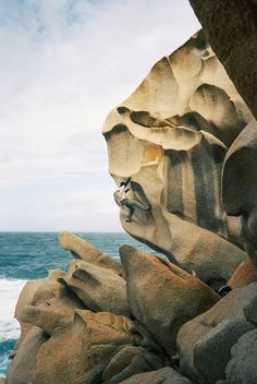 a man climbing up the side of a cliff next to the ocean