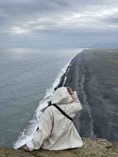 a man sitting on top of a cliff next to the ocean with his head in his hands