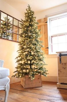 a small christmas tree in a wooden box on the floor next to a white chair