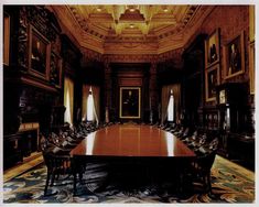 a large wooden table in an ornately decorated room with chairs and paintings on the walls