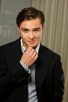 a man in a black suit and white shirt is posing with his hand on his chin