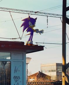 a large purple sonic figure on top of a building next to train tracks and power lines