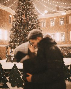 a man and woman standing in front of a christmas tree with lights hanging from the ceiling