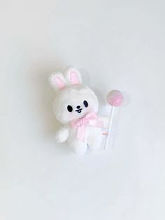 a white stuffed animal with a pink bow holding a lollipop