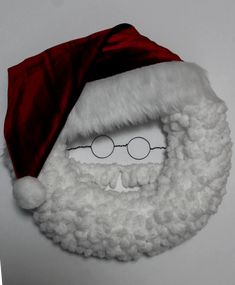 a santa claus beard and glasses on top of a white wall with red velvet hat