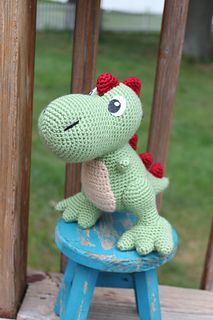 a crocheted dinosaur sitting on top of a blue stool in front of a wooden fence