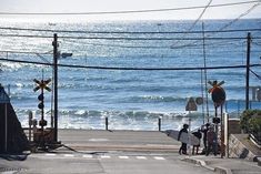 some people with surfboards are walking down the street by the beach and water in the background