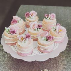 there are many small pink cakes on the cake platter and one has flowers on it