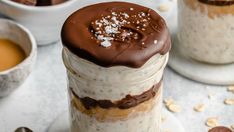 two jars filled with desserts on top of a white table next to cups and spoons