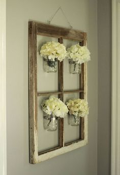 an old window is hung on the wall with vases filled with white flowers and mason jars