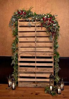 a wooden pallet with candles and greenery on it, sitting in front of a wall