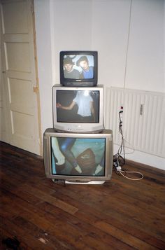 three televisions stacked on top of each other in a room with wood floors and white walls