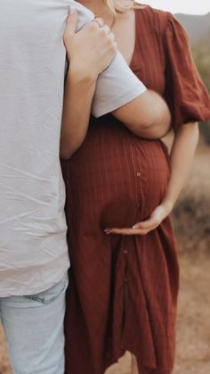 a pregnant woman is holding her husband's belly while they stand in the desert