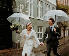 a bride and groom walking down the street holding umbrellas