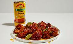 a white plate topped with chicken wings next to a bottle of honey