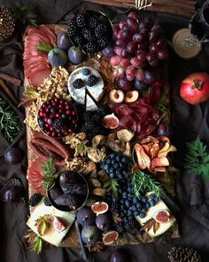 an assortment of fruits, nuts and cheeses on a wooden platter with pine cones