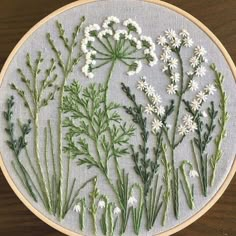 a cross stitch pattern with white flowers and green stems on a wooden surface, in the shape of a circle