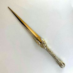 a gold and silver colored metal object on a white surface with an odd shaped handle