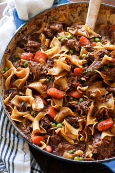 a skillet filled with beef and noodles on top of a blue towel next to a wooden spoon