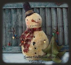 a snowman with a hat and scarf next to a small christmas tree ornament